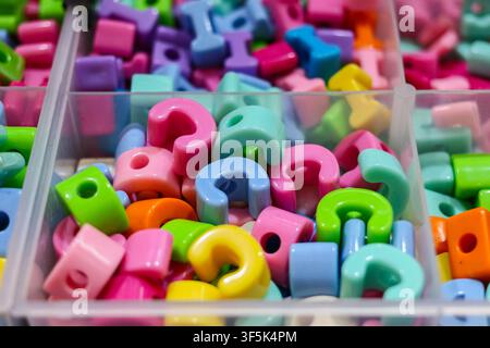 Close-up of colorful plastic alphabet letter beads sorted in a divided craft organizer box, used for handmade jewelry making. Stock Photo
