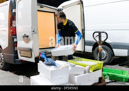 Fishmonger unload fresh fish in foam boxes from a refrigerated delivery van beside a pallet truck, preparing seafood stock for distribution at an outd Stock Photo