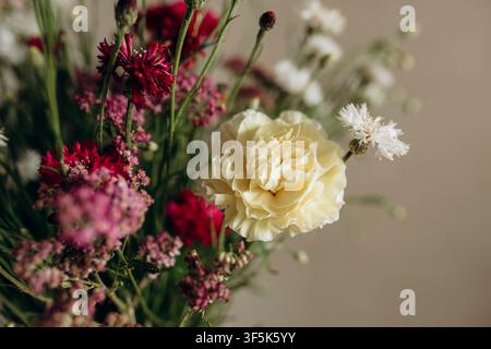 Elegant mixed flower bouquet featuring a cream carnation, burgundy blooms and delicate white wildflowers against a soft neutral background. Stock Photo