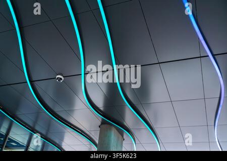Abstract view of a contemporary ceiling with flowing wavy LED light strips in blue and cyan, modern architectural interior detail with sleek panels an Stock Photo