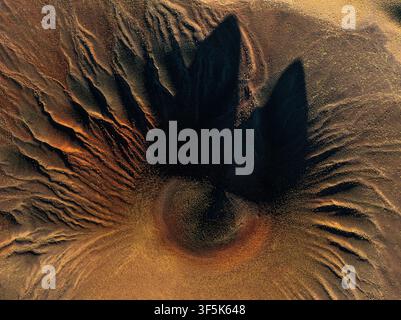 Aerial view of a volcanic cone surrounded by dark lava formations and textured mineral terrain in the high-altitude Puna region of Argentina, revealin Stock Photo