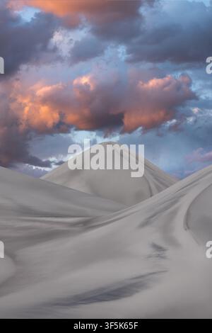 Majestic Saujil Dunes in Catamarca, Argentina, form a remote desert landscape beneath dramatic sunset clouds, with soft pale sand ridges glowing under Stock Photo