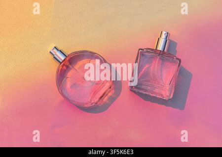 Two transparent non-branded perfume bottles with silver spray nozzles rest on a vibrant pink and orange surface, casting dramatic shadows in a bright Stock Photo