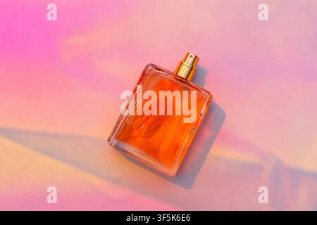 Blank orange perfume bottle mockup with gold spray nozzle arranged on a bright pink and peach background. Soft sunlight creates long shadows for a col Stock Photo