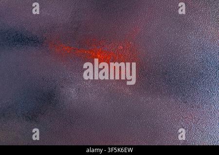 Close-up abstract art texture featuring a dark purple and gray surface with a vivid red-orange accent. The grainy pattern creates a dramatic autumn-in Stock Photo