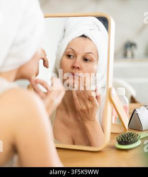Middle-aged woman examining her facial skin looking in the mirror put on the table Stock Photo