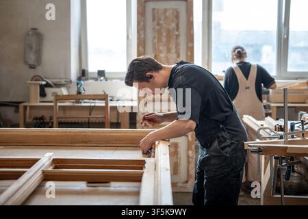 Concentrated craftsman working with antique wooden window frame at workplace in renovation studio. Stock Photo