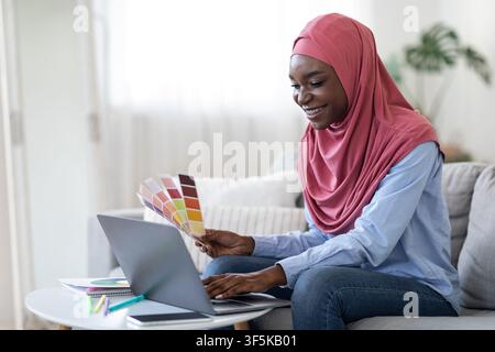 Black Muslim Woman Designer Using Laptop And Holding Color Swatch At Home Stock Photo