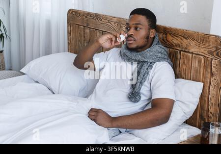 Sick African Man Using Nasal Spray Sitting In Bed Indoor Stock Photo