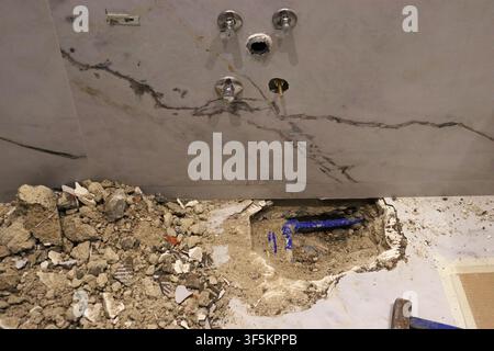 Exposed plumbing and broken concrete beneath a bathroom vanity during renovation work. Interior construction scene showing repair, demolition and home Stock Photo