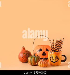 Halloween festive party decorations, candy bowl, pumpkins, funny mug with drinking straw on orange background. Square composition with copy space. Stock Photo