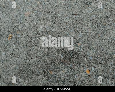 A flat top-down view of an exposed aggregate concrete surface with fine pebbles, stones, and gray cement texture. Stock Photo