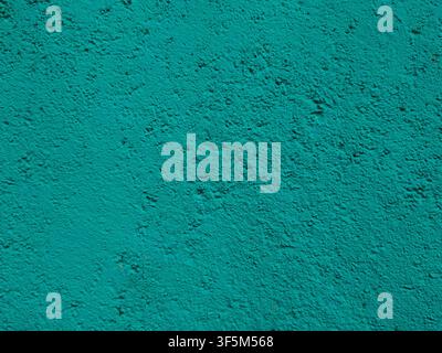 A uniform, textured wall surface coated in bright teal stucco paint showing fine grain and bumpy stipple patterns. Stock Photo