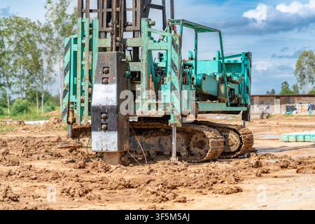 Heavy-duty tracked piling machine driving concrete piles into the soil at a building construction site. Stock Photo
