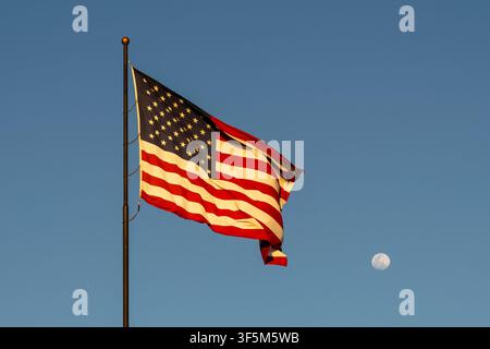 Flag of the United States waving in the wind with blue sky and moon in background. Stock Photo