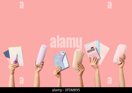 Multiple hands holding various pastel school and office supplies against a pink background education and creativity, the items are arranged on a pink Stock Photo