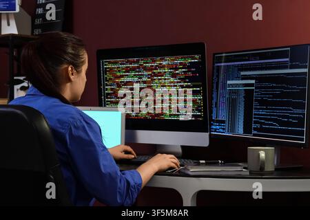 Female programmer working on multiple computer screens with colorful code at a dark desk, the woman is focused on software development and data analys Stock Photo