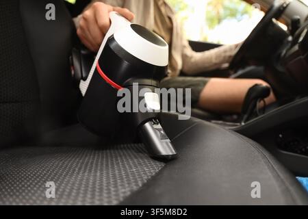 Person cleaning car interior with a portable handheld vacuum cleaner, automotive detailing and maintenance concept, the focus is on the cleaning proce Stock Photo