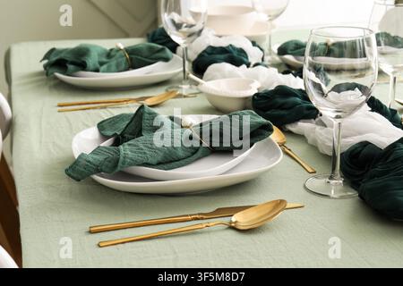 Elegant table setting with green tablecloth, white plates, dark green napkins, and gold cutlery for a special occasion Stock Photo