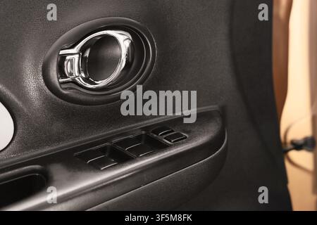 Modern car interior with chrome door handle and power window controls on a black textured panel, the textured black panel provides a sleek and contemp Stock Photo