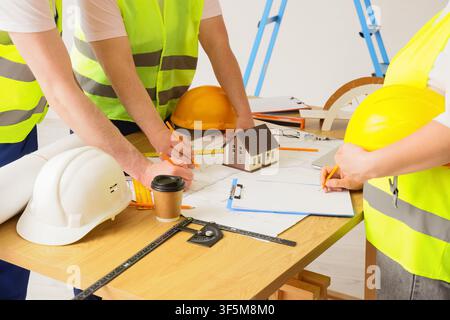 Architects and engineers reviewing blueprints with a house model, construction planning and real estate development, the team is collaborating on desi Stock Photo