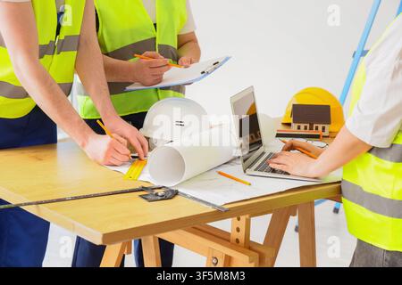 Construction workers in safety vests collaborating on building plans and architectural blueprints with a laptop and hard hats Stock Photo