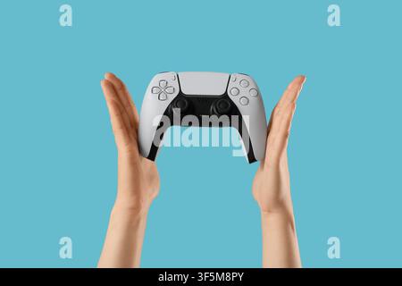 Hands holding a modern white video game controller with black accents, gaming and entertainment concept on a blue background Stock Photo