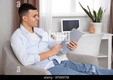 Young man reading magazine in armchair at home Stock Photo