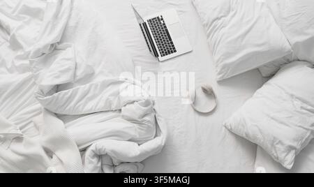 Overhead view of a laptop and headphones on a white unmade bed, remote work and relaxation Stock Photo