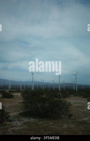 Wind turbines line a hazy mountain ridge above desert scrubland, California Stock Photo