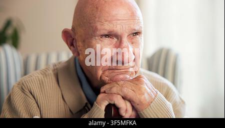 Thinking, sad and senior man in home for nostalgia, sadness and lonely with grief in retirement. House, walking stick and elderly person with Stock Photo