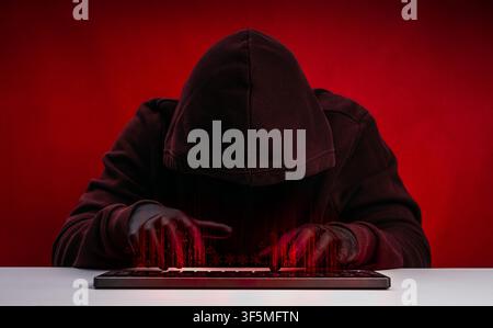 Anonymous hacker in dark hoodie using keyboard computer with digital code overlay on red. Cyberattack, hacking, cybersecurity threat, ransomware, data Stock Photo