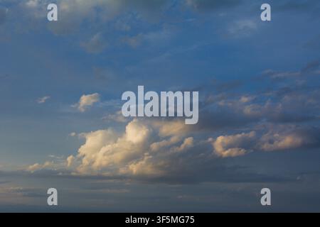 Expansive sky with scattered white clouds illuminated by golden sunlight during late afternoon with shades of blue and gray creating a serene and peac Stock Photo