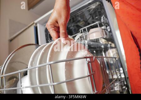 Hand places plates in dishwasher Stock Photo