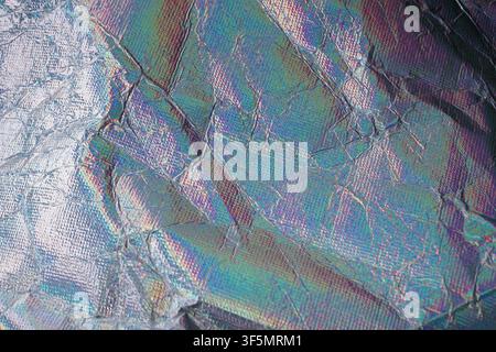 Close-up of wrinkled holographic foil featuring iridescent rainbow colors and metallic texture. Ideal for futuristic, abstract, and creative design ba Stock Photo