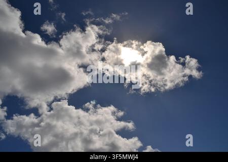 Sunlight breaking through silver-lined cumulus clouds in a deep blue sky Stock Photo