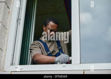 Black Man Fixing Window Frame with Tool during House Renovation Stock Photo