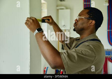 Black Man Measuring Wall with Tape during House Renovation Stock Photo