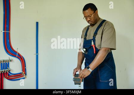 Black Man in Overalls Using Laser Level for House Renovation Stock Photo