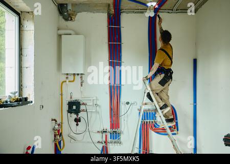Man Standing on Ladder Installing Pipes during House Renovation Stock Photo