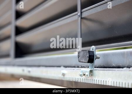 Close-up of magnetic limit switch bracket mounted on modern steel automatic sliding gate gear rack system, ensuring precise motorized stopper alignmen Stock Photo