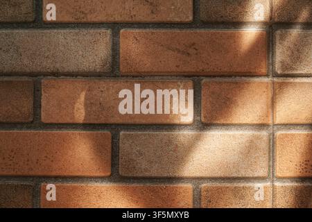 Close-up of a weathered terracotta brick tile wall featuring natural sunlight and diagonal shadow patterns. Ideal for architectural and design backgro Stock Photo