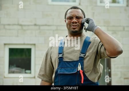 Black Builder Talking on Smartphone at House Renovation Site Stock Photo