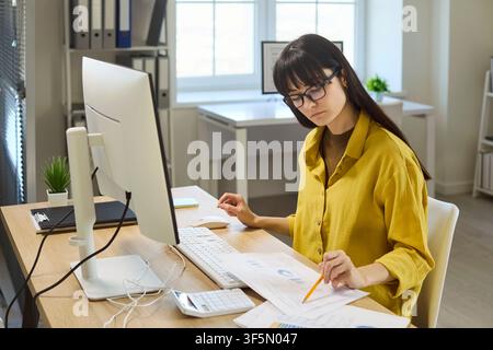 Focused woman accountant analyzing paperwork at office computer with calculator Stock Photo