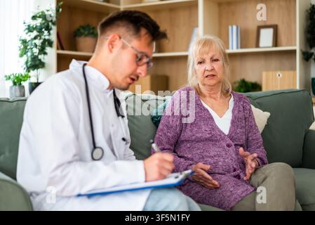 A healthcare professional carefully documents an elderly patient's concerns as she discusses her health issues during an in-home medical appointment. Stock Photo