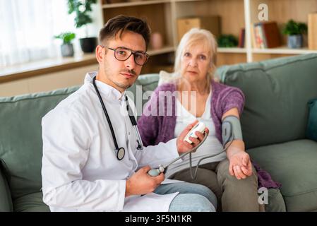 A doctor performs a blood pressure check for a senior patient using a digital monitor during an in-home consultation. Stock Photo