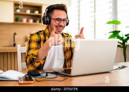 Happy young man is working at home. He is using laptop for online communication. Stock Photo