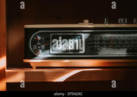 Close up shot of a retro analog flip clock radio resting on a wooden surface in warm morning sunlight showing 9:31 with frequency dials and controls v Stock Photo