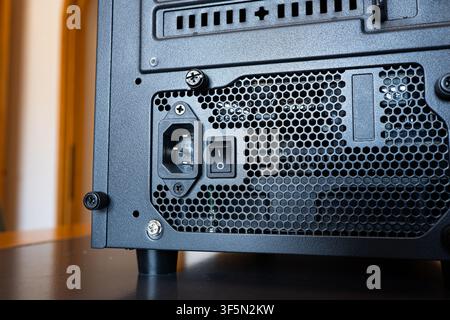 Close up shot of the back of a desktop computer case showing the power supply unit with power socket, toggle switch, and mesh ventilation. Stock Photo