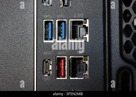 Macro close up shot of a computer motherboard rear IO panel displaying blue USB 3.0 ports, red USB port, Type-C port, and 1G and 2.5G Ethernet RJ45 ja Stock Photo